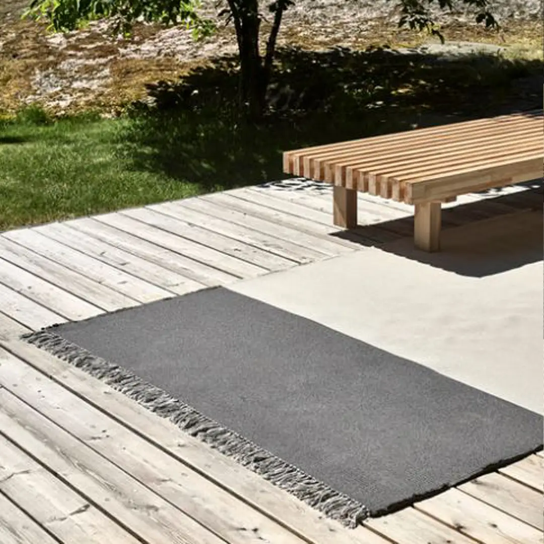 Outdoor wooden deck with rug and bench in sunlight