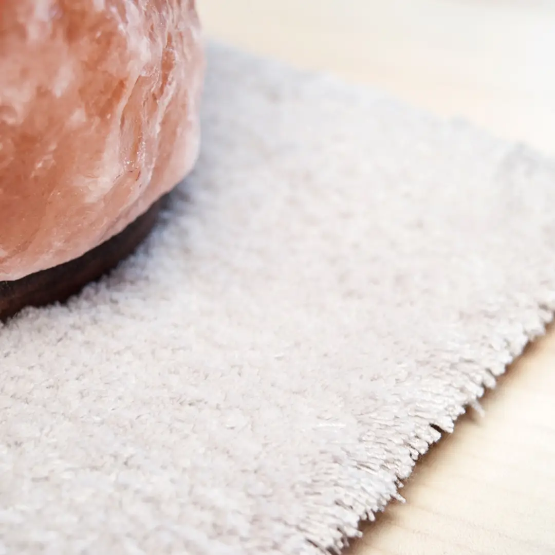 Salt lamp on wooden base on white textured rug