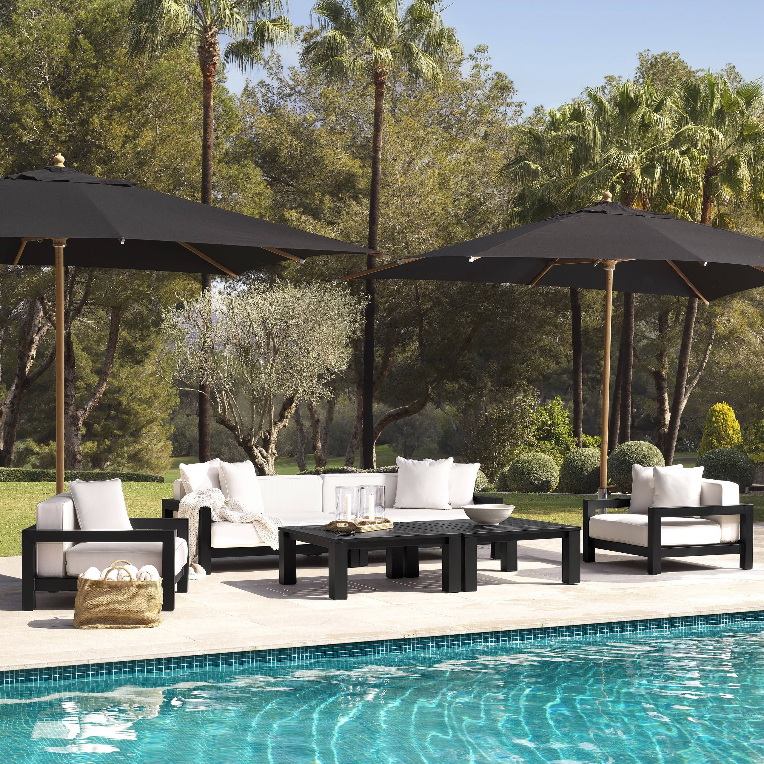 Luxurious poolside patio furniture under umbrellas surrounded by trees