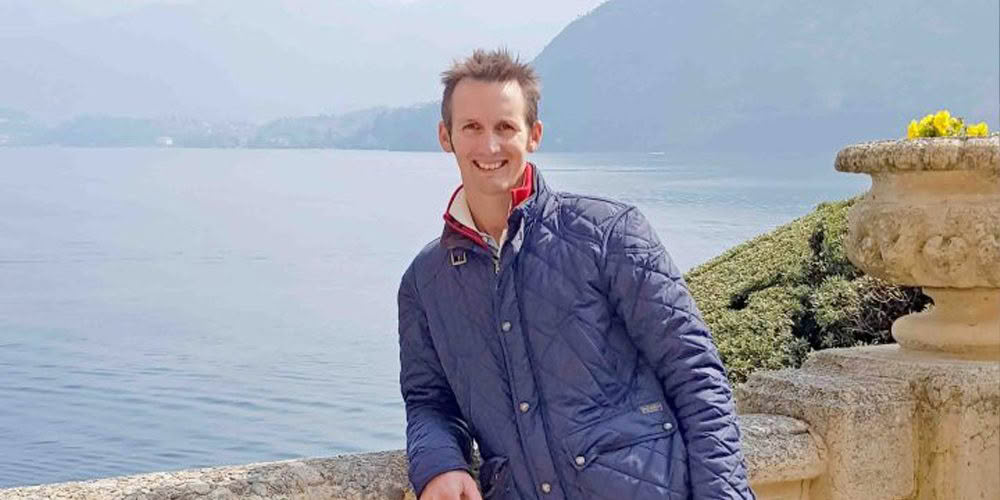 Man smiling by lake with mountains in background