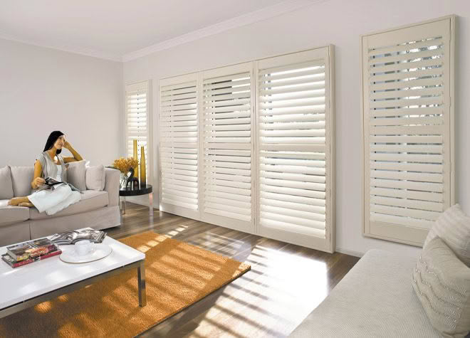 Woman relaxing in sunlit room with large white shutters