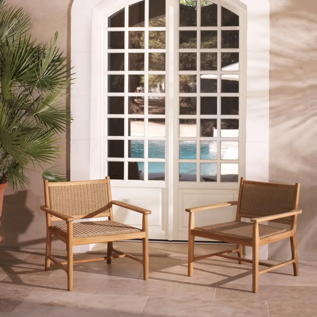 Wooden chairs by poolside patio door with palm plant