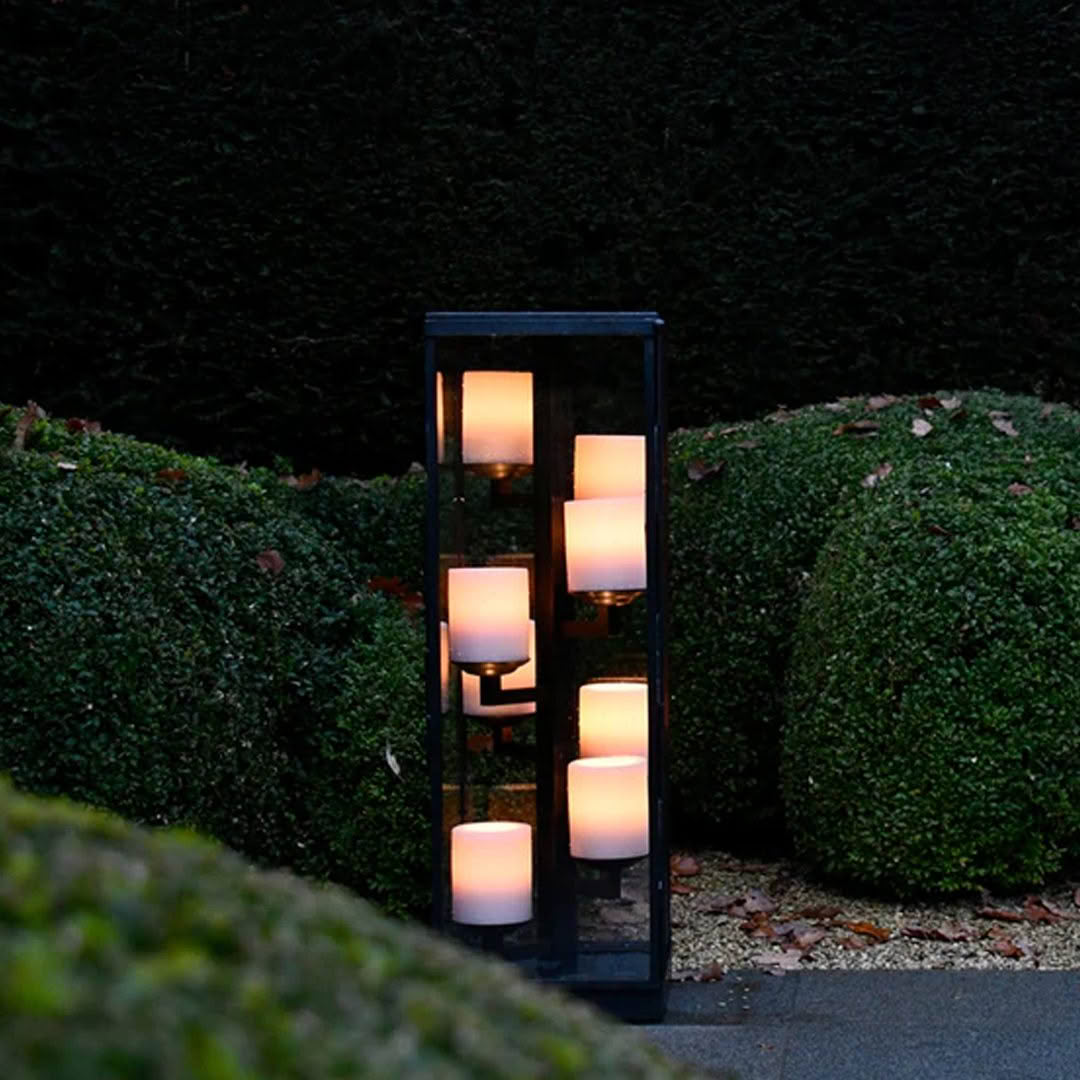 Tall outdoor lantern with multiple glowing candles at dusk