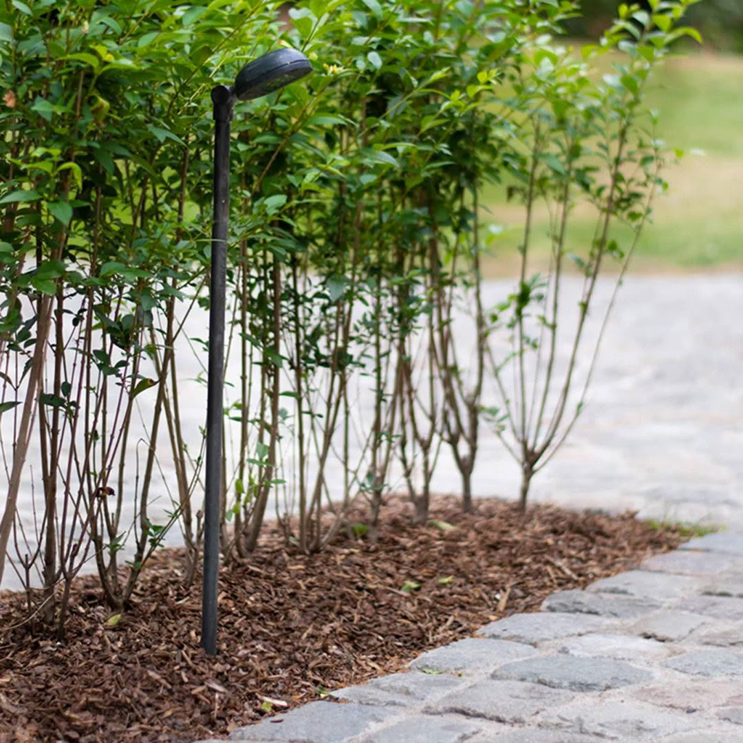 Solar garden light beside cobblestone path and shrubs