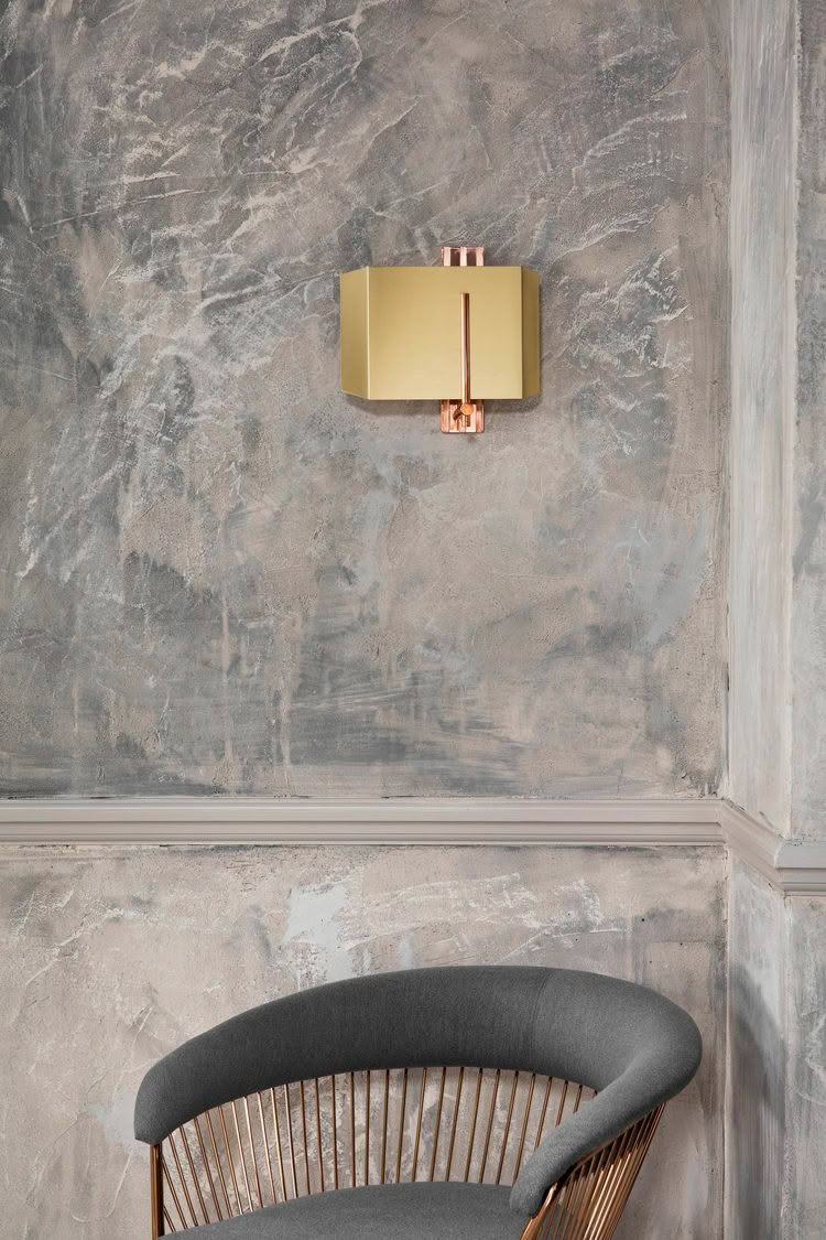Modern gold wall sconce above stylish gray chair