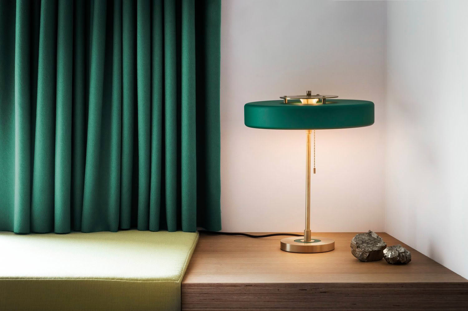 Modern lamp on desk beside teal curtains and bed