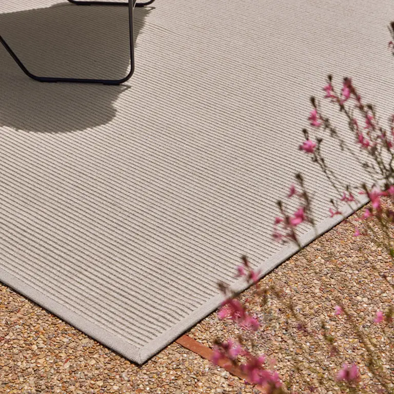 Outdoor rug with chair and pink flowers on gravel