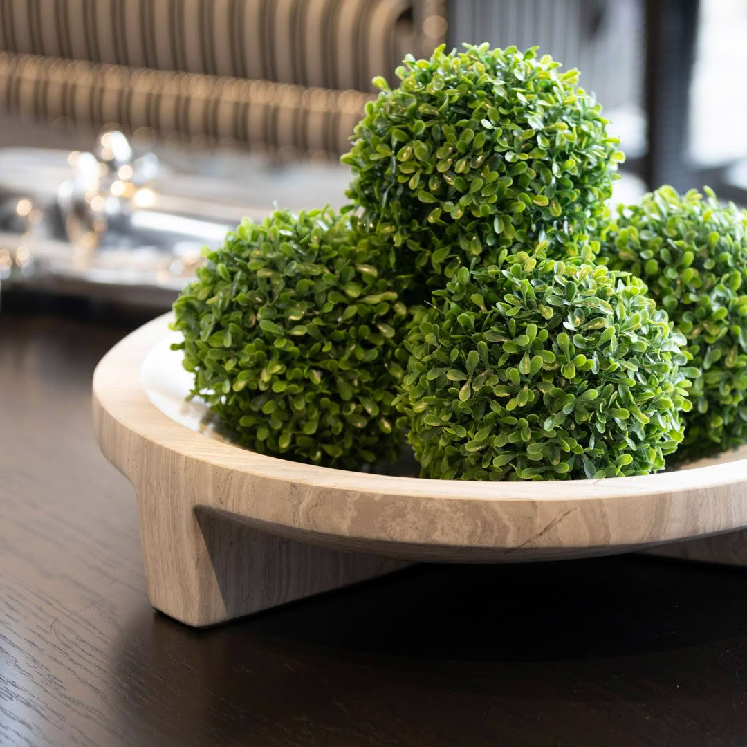 Decorative green topiary balls in marble bowl on table