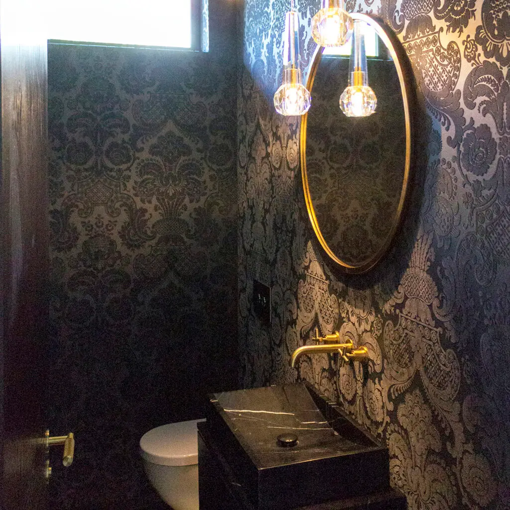 Elegant dark bathroom with ornate wallpaper and gold accents