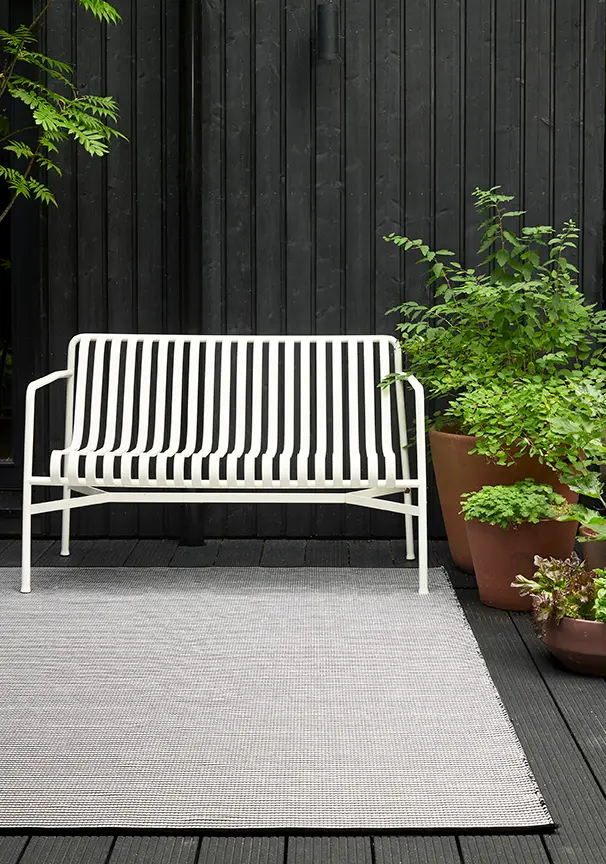 White bench on a black deck surrounded by plants