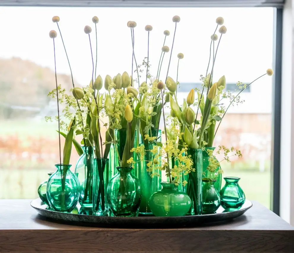 Variety of flowers in green glass vases on tray