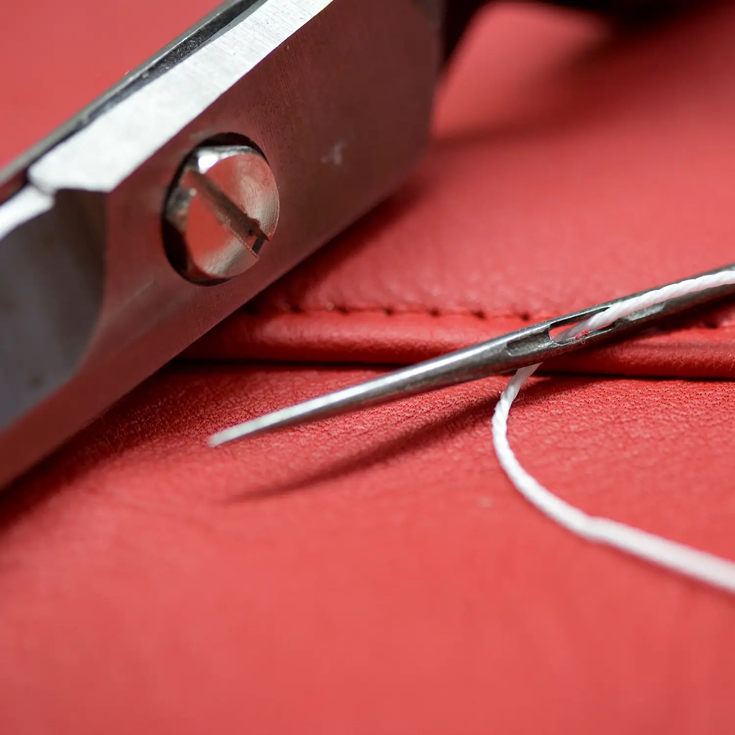 Close-up of needle and pliers on red leather