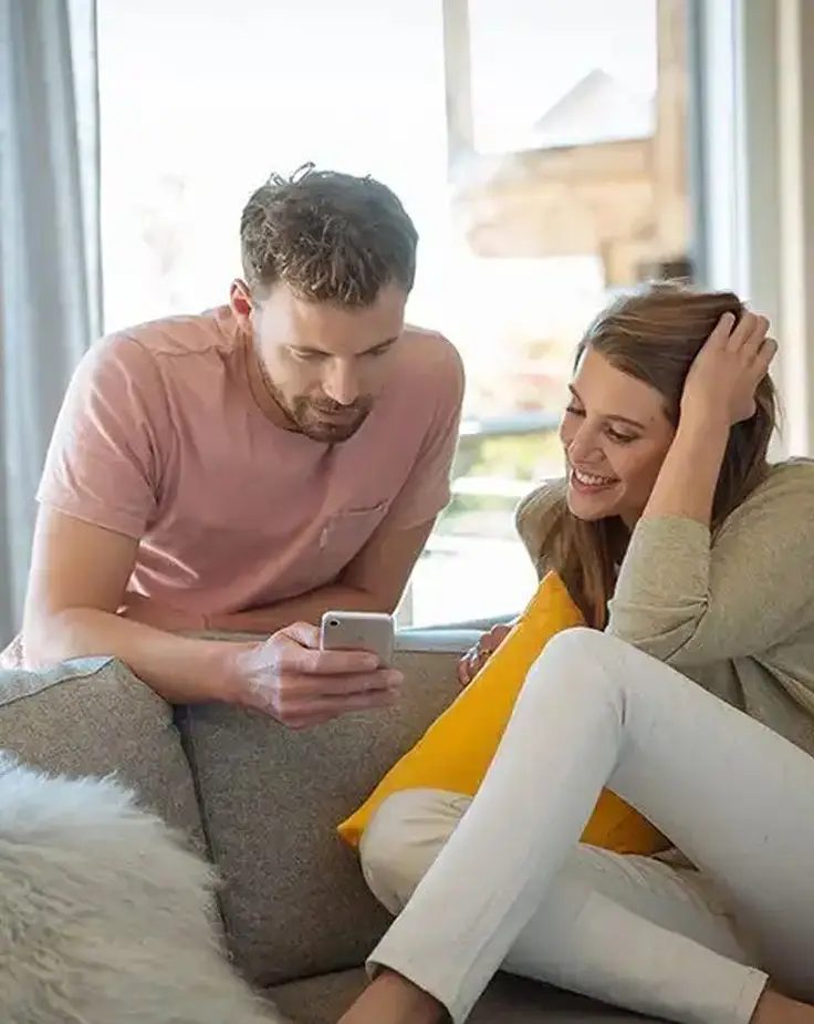 Couple lounging on sofa, browsing smartphone together