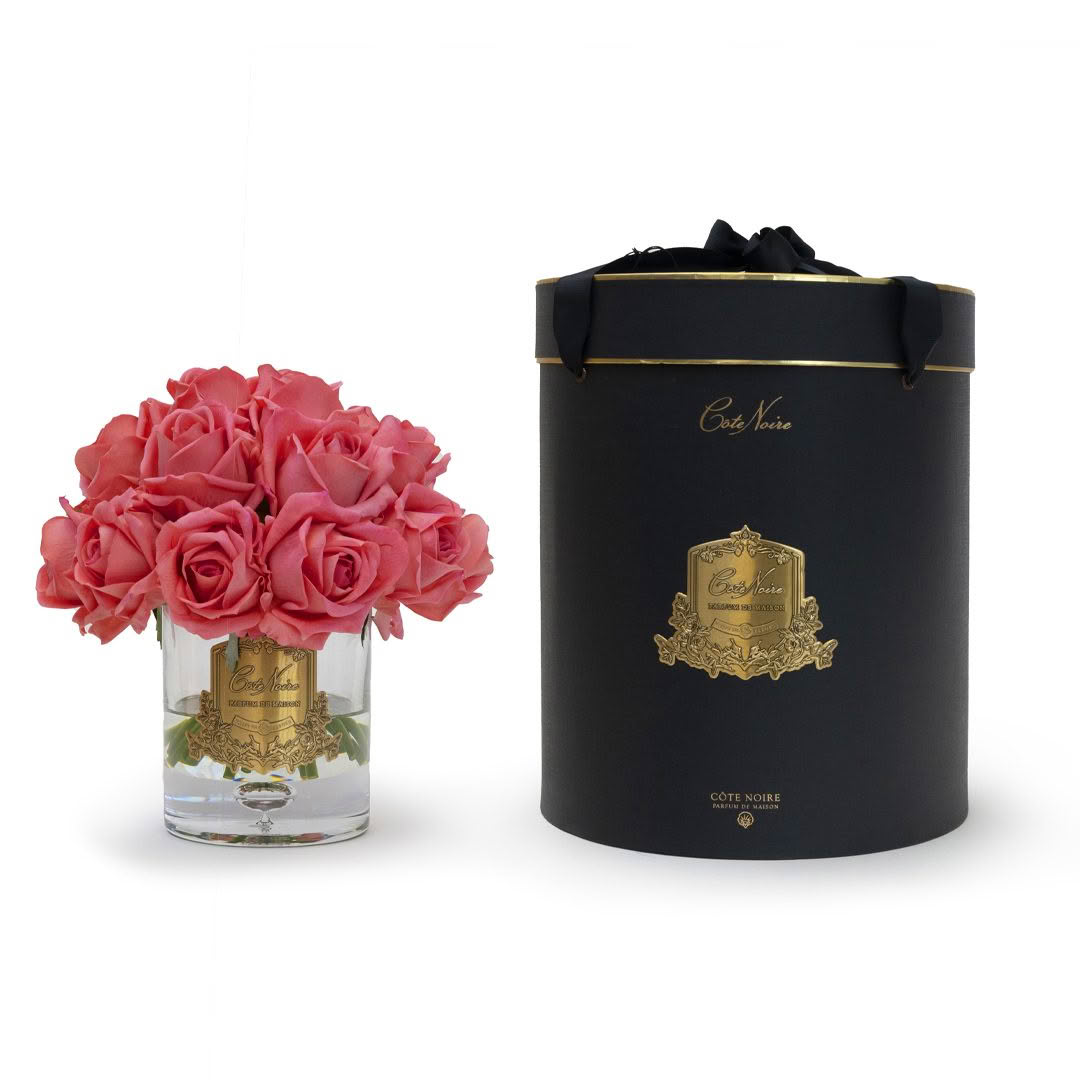 Pink roses in glass vase beside black gift box