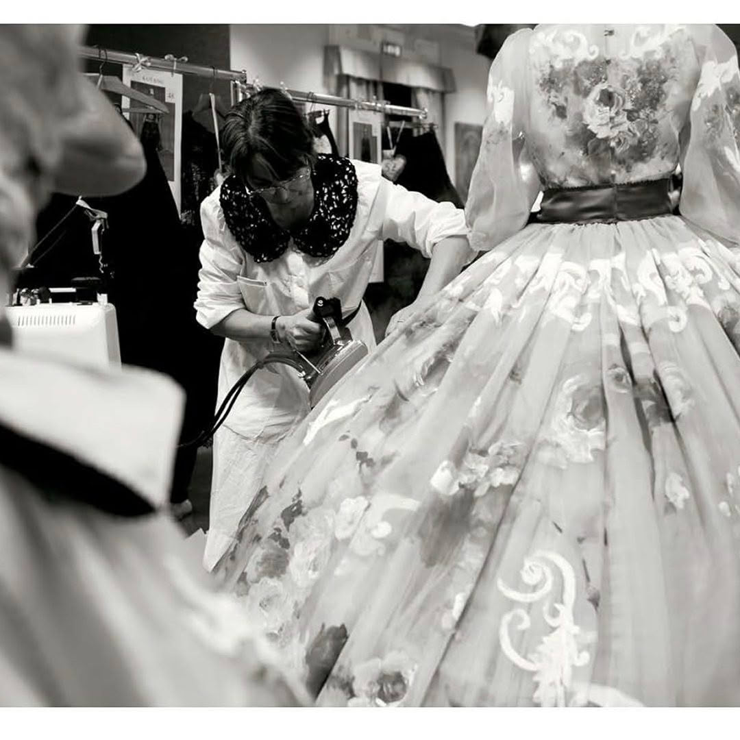 Designer steaming floral gown in busy workshop