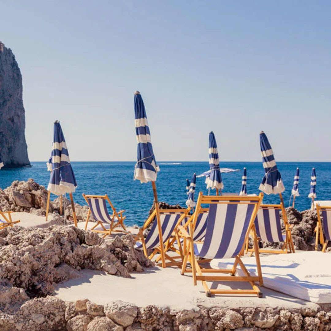 Striped beach chairs and umbrellas by rocky seaside