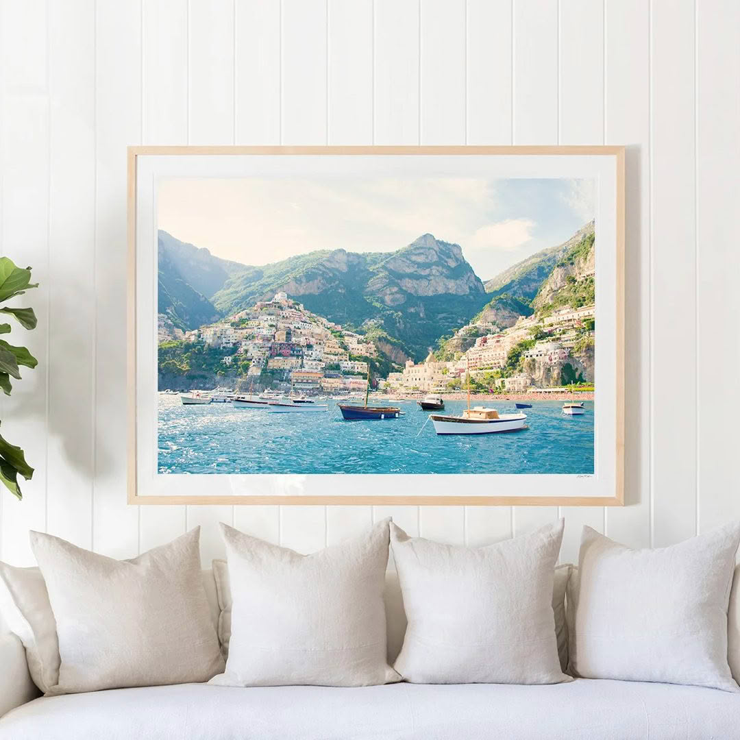 Framed coastal landscape painting above couch in bright room