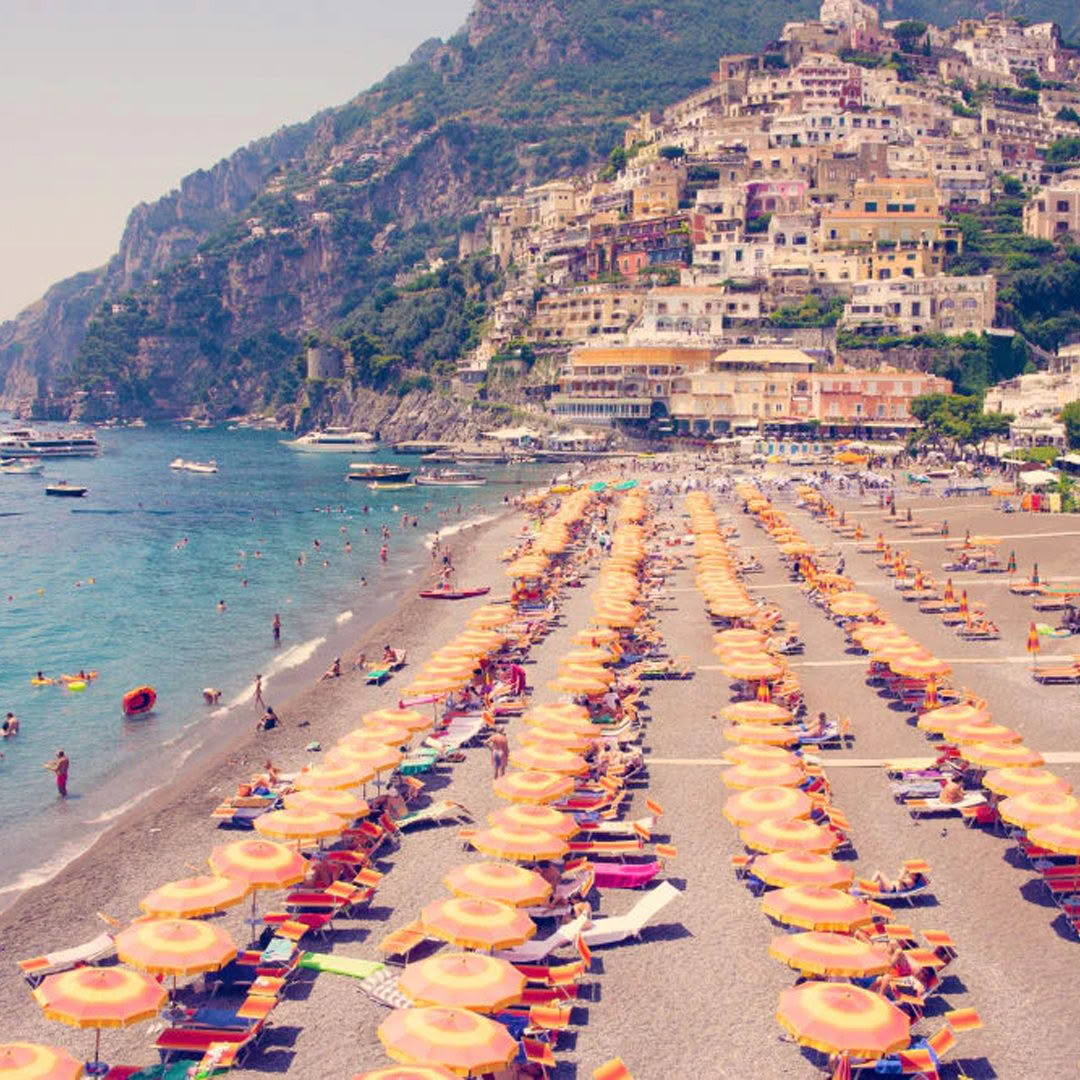 Crowded beach with colorful umbrellas and cliffside buildings