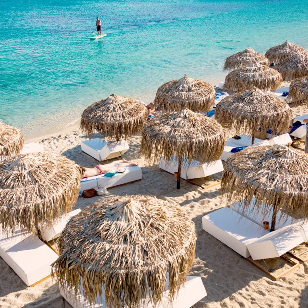 Tropical beach with straw umbrellas and paddle boarder
