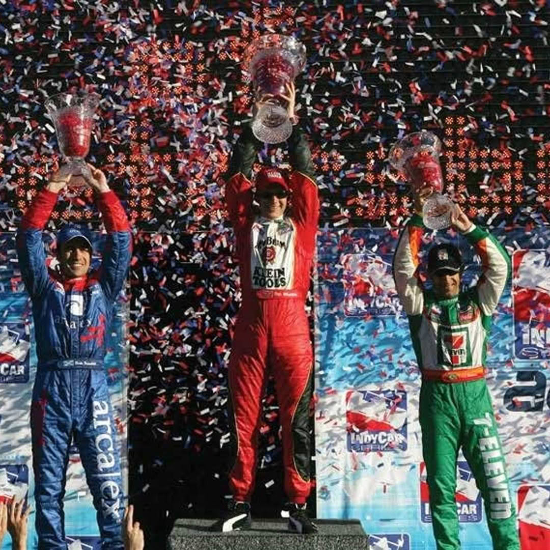 Three race car drivers holding trophies amid confetti