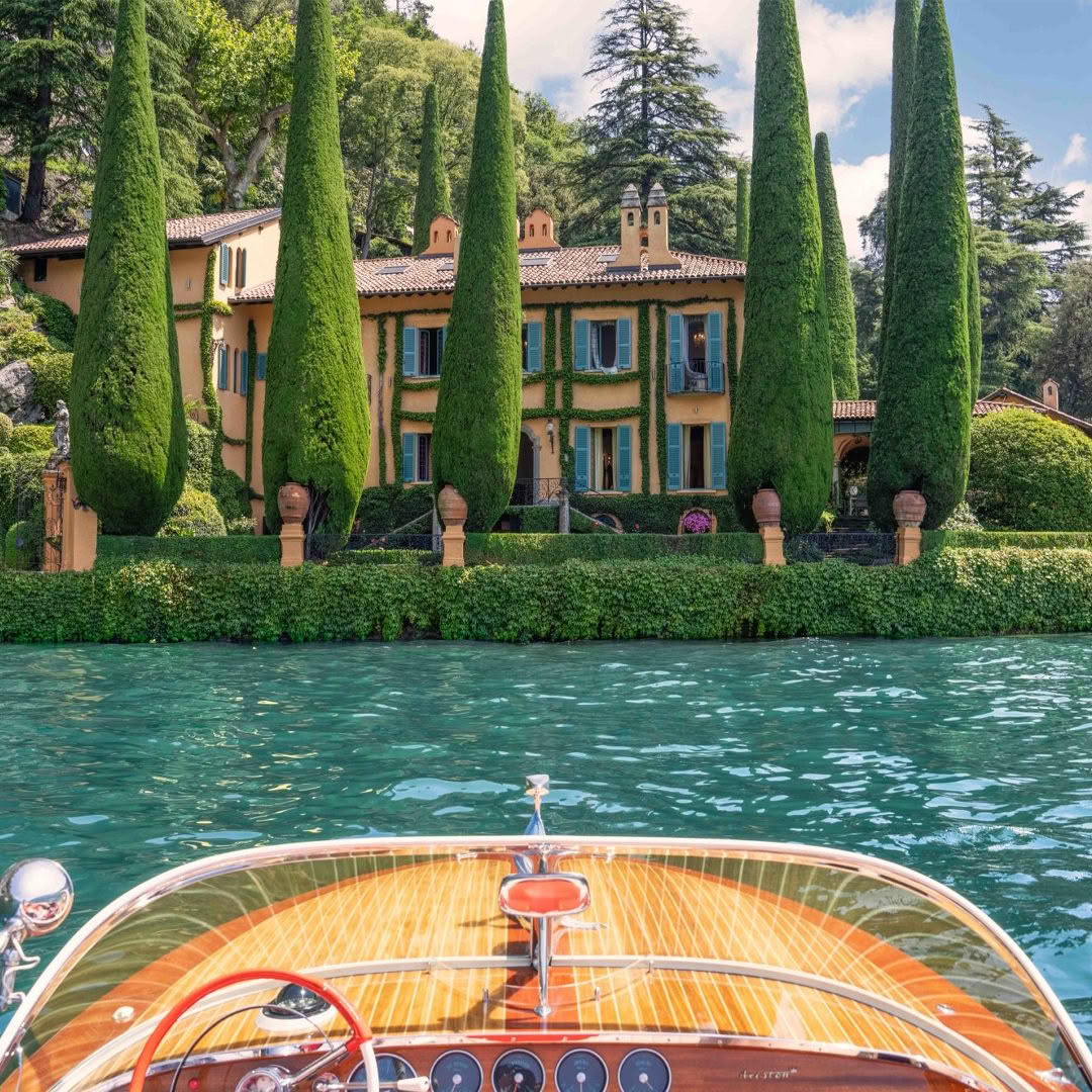 Luxury wooden boat approaching lush lakeside villa