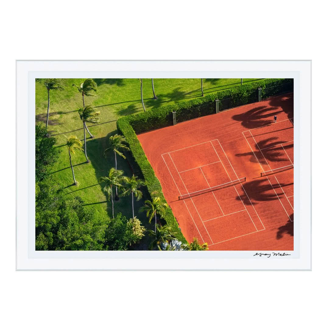 Aerial view of red clay tennis court surrounded by palm trees