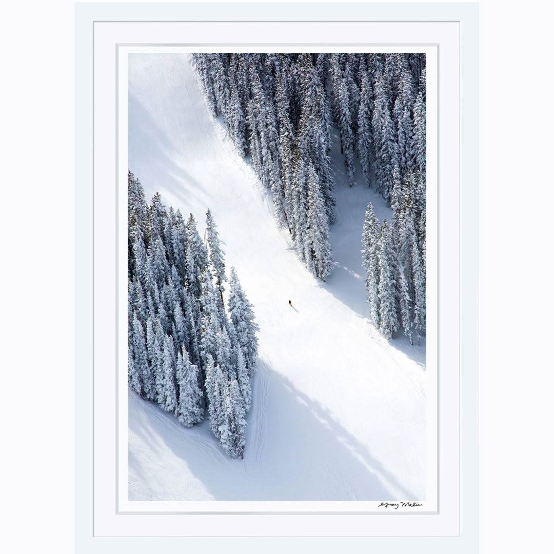 Skier descending snow-covered mountain slope among trees