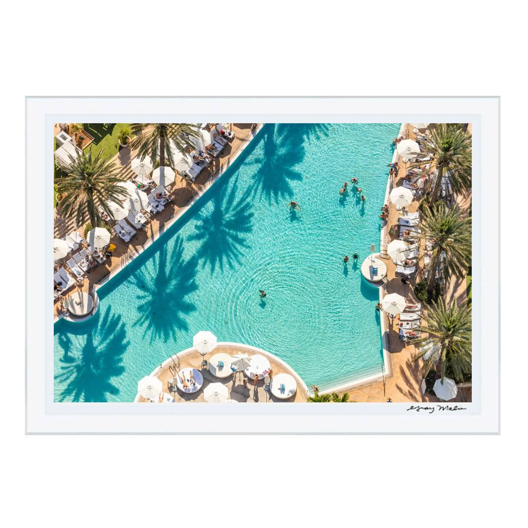 Aerial view of resort pool with swimmers and palm shadows