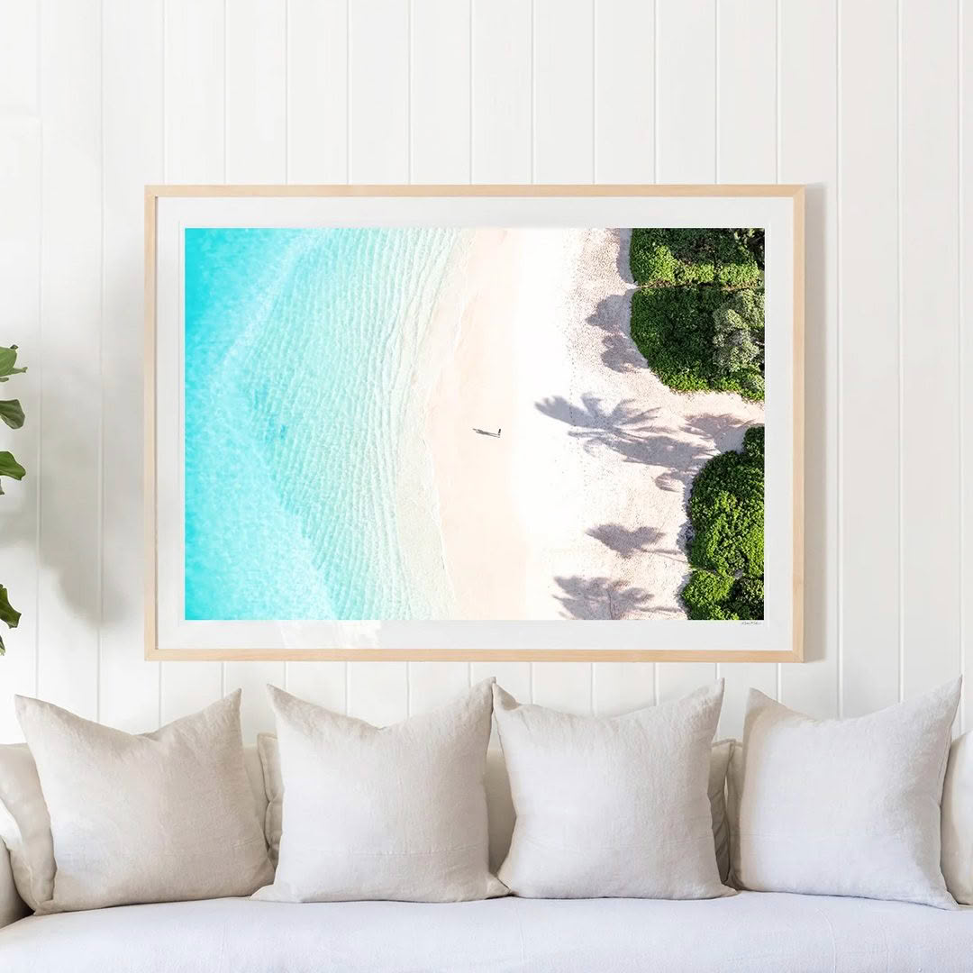 Framed beach aerial view artwork above white sofa