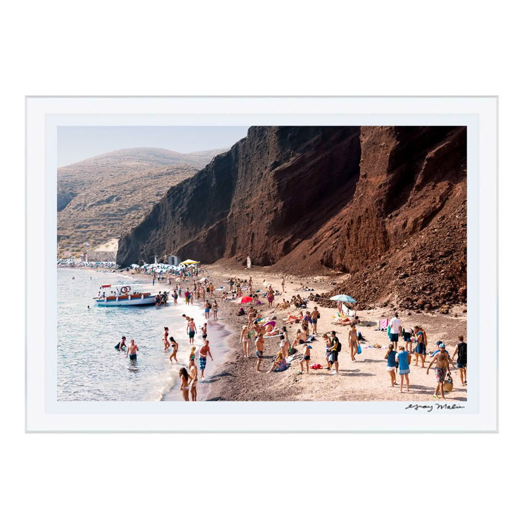 Crowded beach near large red cliff with boat offshore