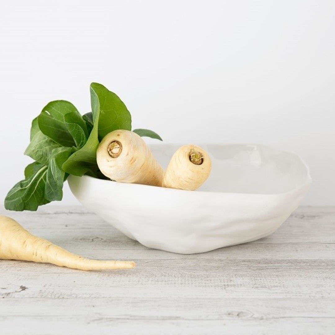 Parsnips and green leaves in white ceramic bowl