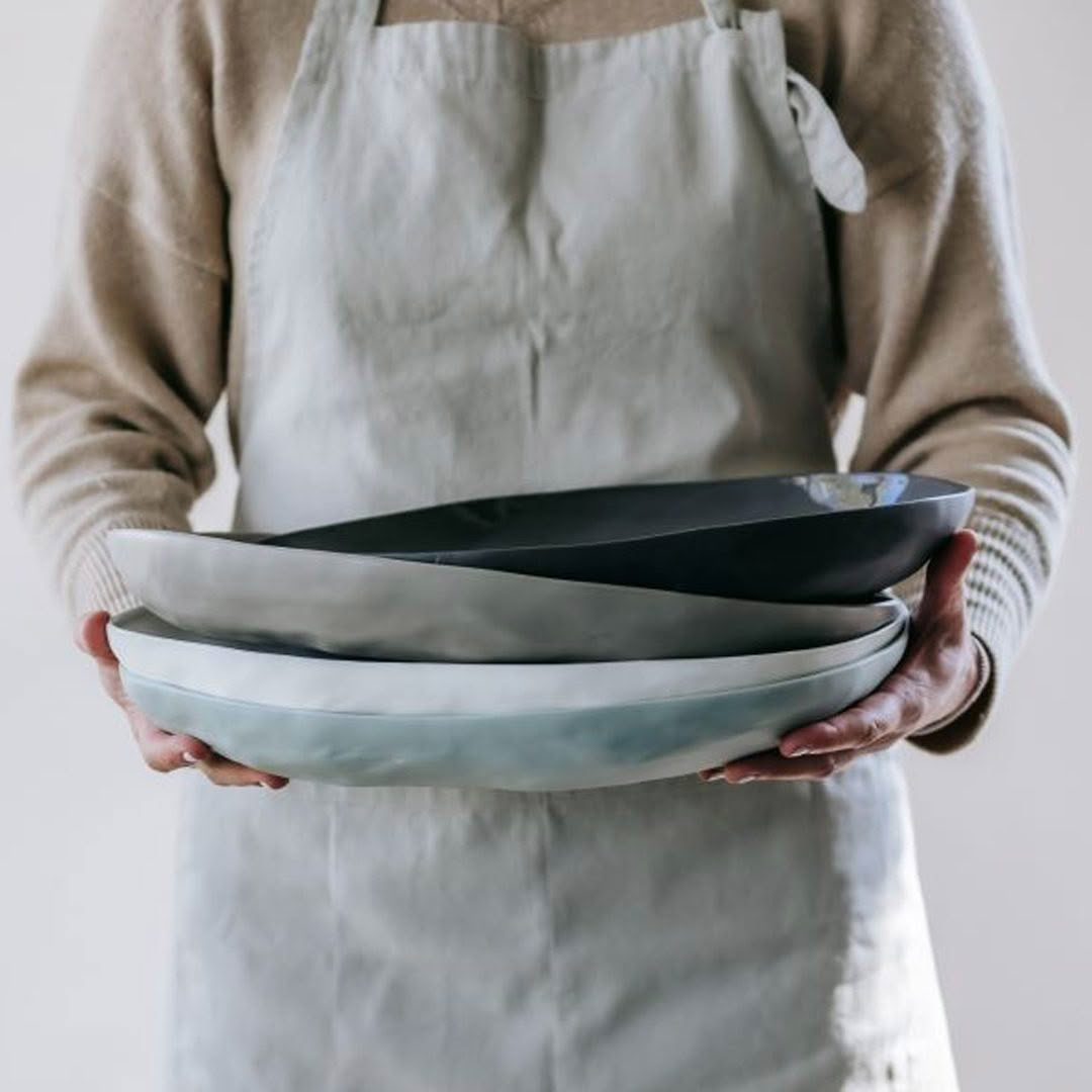 Person in apron holding stack of ceramic plates