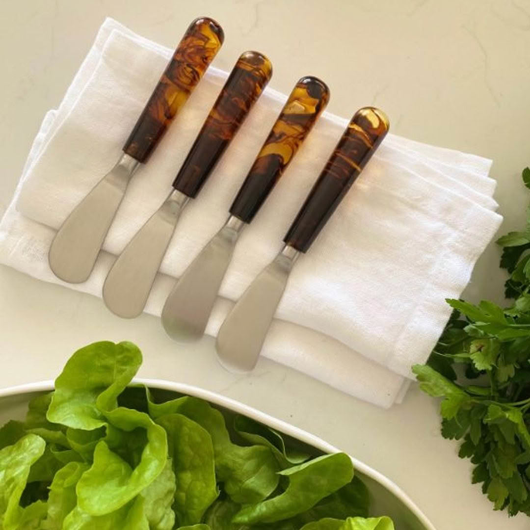 Cheese knives set on white napkin, fresh greens beside