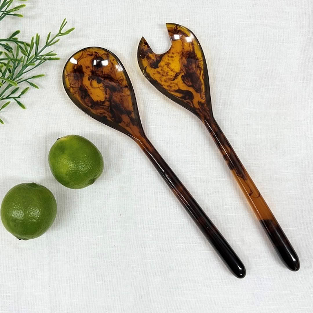 Tortoiseshell salad servers on white cloth with lime and rosemary